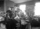 Hattaffär, 1909, troligen Växjö. Ett antal kvinnor jobbar eller tittar på en mängd hattar.