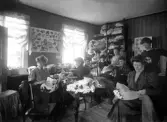 Hattaffär, 1909, troligen Växjö. Ett antal kvinnor sysslar med att tillverka/sy ett antal damhattar.