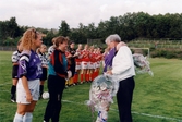 Kvarnbyvallen i Mölndal, år 1996. I samband med en fotbollsmatch mellan Jitex BK och Landvetter IF delas blombuketter ut till Jitex-spelarna Pernilla Bowall, Eva Larsson och Camilla Svensson. Matchen slutade 1-1.