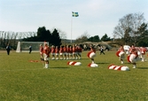 Kvarnbyvallen i Mölndal, år 1997. Fotbollslaget Jitex BK värmer upp inför en match mot Lotorps IF, vilken slutade med resultatet 0-1. Mölndals Paradorkester underhåller på fotbollsplanen.