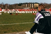 Kvarnbyvallen i Mölndal, år 1997.  Mölndals Paradorkester underhåller på fotbollsplanen. En fotbollstränare sitter och tittar på.