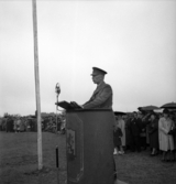 Försvarets dag. Foto av trupprevy på övningsfältet. Överste Sven Allstrin talar (i regnväder).