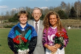 Porträtt av en man med Mallbackens målvakt och Jitex Pernilla Bowall bredvid sig. Spelarna har fått blommor. Fotografi taget i samband med att fotbollslaget Jitex BK spelade match mot Mallbackens IF på Kvarnbyvallen i Mölndal, april 1993. Matchen slutade 2-1 till Jitex.