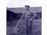 Karl Wiktor Johansson stående på stenlagd gårdsplan med en skyffel. Marbogård, Sällstorp 6.
