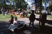 Trampbilar väntar vid jänvägsbommar på Stora Holmen då lilleputtåget ska passera, 1989