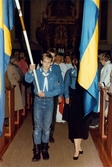 Kröningen av Mölndals Lucia i Fässbergs kyrka i december 1985. Lucian och tärnorna tågar ut ur kyrkan. Före går två scouter som fanbärare.