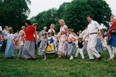 Midsommarfirande vid Gunnebo slott i Mölndal på 1990-talet. Små och stora deltar i dansen kring midsommarstången.