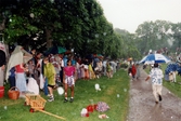 Midsommarfirande vid Gunnebo slott i Mölndal, okänt årtal. Vuxna och barn tar skydd undan regnet med vad som finns till hands.