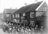 Kvarter Friden, Drottninggatan mellan Färgaregatan och Torggatan. Fastigheten riven 1910. Musikkåren med blåsintrument och trummor, tågar nedför gatan inför åskådare.