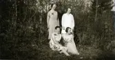 Fyra uppklädda kvinnor i Albäck utomhus, troligen tidigt 1930-tal. Anna Gabrielsson står till vänster och Selma i Alobäck till höger. Nedanför dem sitter Anna Sjögren till vänster och Linnea Molin till höger (se även EA0849).