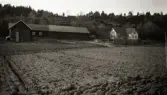 Karl Larssons gård i Veddige nedanför den bergiga åsen, Ekonomibyggnad och bostadshus med plöjda åkrar i förgrunden.