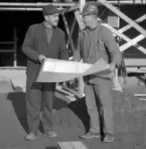 Två män står och läser en ritning på taket till köpcentret Rosen i Huskvarna.