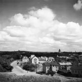 Vy från Varbergs fästning längs Strandgatan åt nordöst. Till höger ses nedre delen av kv Platsarna och därefter gaveln till Varmbadhuset, uppfört 1925, och kv Skepparen. I gatans fond ses vattentornet och till höger skjuter kyrktornet upp ur grönskan.