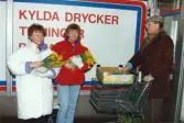 Medlemmar i fotbollsföreningen Jitex BK delar ut blommor till folk i Mölndals centrum i mars 1992. Två kvinnor och en man med kundvagn är redo att börja dela ut blommor utanför K-marknad på Brogatan.