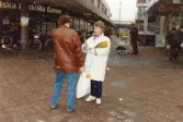 Medlemmar i fotbollsföreningen Jitex BK delar ut blommor till folk i Mölndals centrum i mars 1992. En kvinna får blommor i korsningen Brogatan-Nygatan. SEB i bakgrunden.