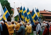 Nationaldagsfirande i Stadshusparken i Mölndal den 6 juni 1999. En samling män håller upp den svenska flaggan samt ett par föreningsflaggor.