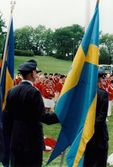 Nationaldagsfirande i Stadshusparken i Mölndal den 6 juni 1999. I förgrunden män som håller upp den svenska flaggan, i bakgrunden Mölndals Paradorkester.