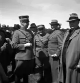 Kamratmötet, I 11. Samling på övningsfältet. Några herrar i uniform (m/23) pratar med några civila i hatt och kostym m.m.