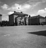 Kamratmötet, I 11. Kanslihuset från kaserngården. Man ser också en del flaggstänger med girlander emelllan.