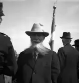 Kamratmötet, I 11. En äldre herre i helskägg, iklädd kostym och hatt.