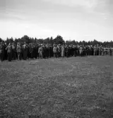 Kamratmötet, I 11. Äldre herrar i kostym och hatt, står uppställda på övningsfältet.