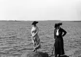 Några sommarklädda kvinnor står på några stenar vid havet.