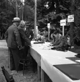 Medborgartåget, 16/6 1940. 
Tecknande av försvarsobligationer. Ett antal herrar har samlats för
att anteckna sig för obligationer. Ett antal banker har representanter
sittande vid ett långt bord.