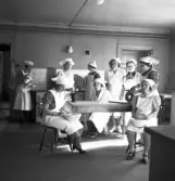 Blindskolan. 
Några unga kvinnor i stora vita förkläden (och hättor), i skolköket.