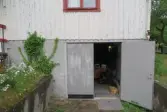 Ingång från trädgården till förråd/garage i källarplan (se 2024_1530), Krokslättsgatan 18 i Mölndal 2023-06-21. Till vänster ses växlighet. Rakt fram ses en del av den vita husfasaden samt en (av två) öppen dörr till förrådet. Fotodokumentation av ett friliggande bostadshus/villa byggt 1932 med fyra (4) våningsplan. Byggnaden har tvättstuga i källaren samt torkvind på övervåningen. Boarea: 140 kvm, totalarea: 1004 kvm. Villan är ombyggd och fördelad på fyra (4) hyreslägenheter.
Relaterade motiv: 2024_1415 - 1541.