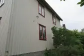 Bostadshusets baksida med dess vitmålade träfasad och fyra fönster med roströda karmar (se 2024_1532), Krokslättsgatan 18 i Mölndal 2023-06-21. Till höger ses växtlighet. Fotodokumentation av ett friliggande bostadshus/villa byggt 1932 med fyra (4) våningsplan. Byggnaden har tvättstuga i källaren samt torkvind på övervåningen. Boarea: 140 kvm, totalarea: 1004 kvm. Villan är ombyggd och fördelad på fyra (4) hyreslägenheter.
Relaterade motiv: 2024_1415 - 1541.