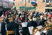 Påskfirande på Mölndals torg lördagen den 3 april 1999. Frälsningsarméns hornmusikkår spelar på den lilla scenen. Påskkärringarna står och lyssnar.