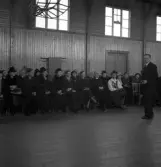 Avslutning vid Grimslövs folkhögskola.
En man i glasögon och kostym, pratar om något framför en sittande publik, med bl a en präst till höger.