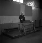 Avslutning vid Grimslövs folkhögskola.
En äldre man i kostym, talar vid katedern/talarstolen i gymnastiksalen.