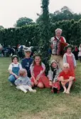 Midsommarfirande vid Gunnebo slott i Mölndal, år 1999. Porträtt av några flickor och pojkar samt en man med dragspel vid midsommarstångens fot.