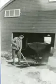 Emil Söderhäll vaskar flakar på isen framför ett båthus, 1950-tal.