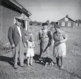 Alfhild Ericsson t.h. står med en hundvalp, en man, en kvinna och ett barn. Flera hus i bakgrunden, 1929.