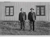 Johan Johansson t v och Julius Johansson t h står framför en husvägg. Lelle-Larsa, fastighet Skärte 4, Rolfstorp.