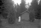 Kvinna vid en timmerstuga, 1920-tal