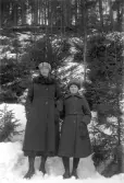 Kvinna och flicka klädda i vinterrockar och mössor framför en snöig skog