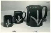 Muggar 3334/1-2 och kanna 3335 från Bo Fajans, formgivare Eva Jancke-Björk, 1900-talets mitt. Svartglasyr med relief av vete.