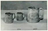 Muggar 3334/1-2 och kanna 3335 från Bo Fajans, formgivare Eva Jancke-Björk, 1900-talets mitt. Reliefdekor med en lagerkrans runt årtalet 1940.