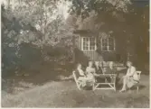 Selma (1887 - 1971) och Efraim Magnusson (1876 - 1960) sitter och fikar tillsammans med sommargäster i trädgården, Apelgården 