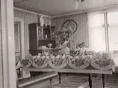 Festligt dukat kaffebord med en stor hortensia i mitten. Salongen har en kraftig, målad taklist och dekorationsmålning längs takkanten. Förmodligen i Rolfstorp eller Skällinge som var fotografens hemvist.