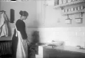 Kvinna gräddar våfflor på vedspis i köket, 1920-tal