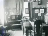 Rumsinteriör med piano och pianopall, bord och stolar, draperier och i rummet intill syns en soffa och karmstolar mm. troligen från Centralpalatset i Gävle stad.