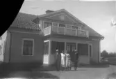 Familj framför hus med stor veranda, 1920-tal
