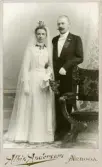 Brud i vit klänning, vita handskar och myrtenkrona bredvid sin brudgum i Arboga, omkring 1900