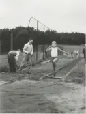 Elever från Kålleredskolan (senare Brattåsskolan) har idrottsdag på Stretereds idrottsplats 1950-tal. En elev hoppar längdhopp och till vänster står två elever för att mäta resultatet.