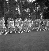 Gymnastikuppvisningen, 25/5 1941. 
Kvinnliga gymnaster tågar in på Värendsvallen. Genom skogen i 
bakgrunden skymtar några av kasernerna på I 11.