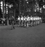 Gymnastikuppvisningen, 25/5 1941. 
Manliga gymnaster tågar in på Värendsvallen, med en uniformsklädd
herre i täten.